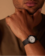 Casio MQ-24-7BLLEG Analoguhr am Handgelenk einer Person vor braunem Hintergrund